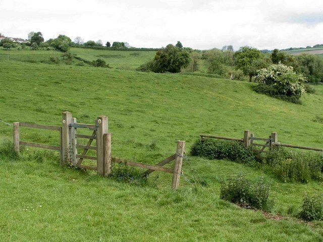 A rural landscape with rolling green hills, a wooden gate, and a fence.