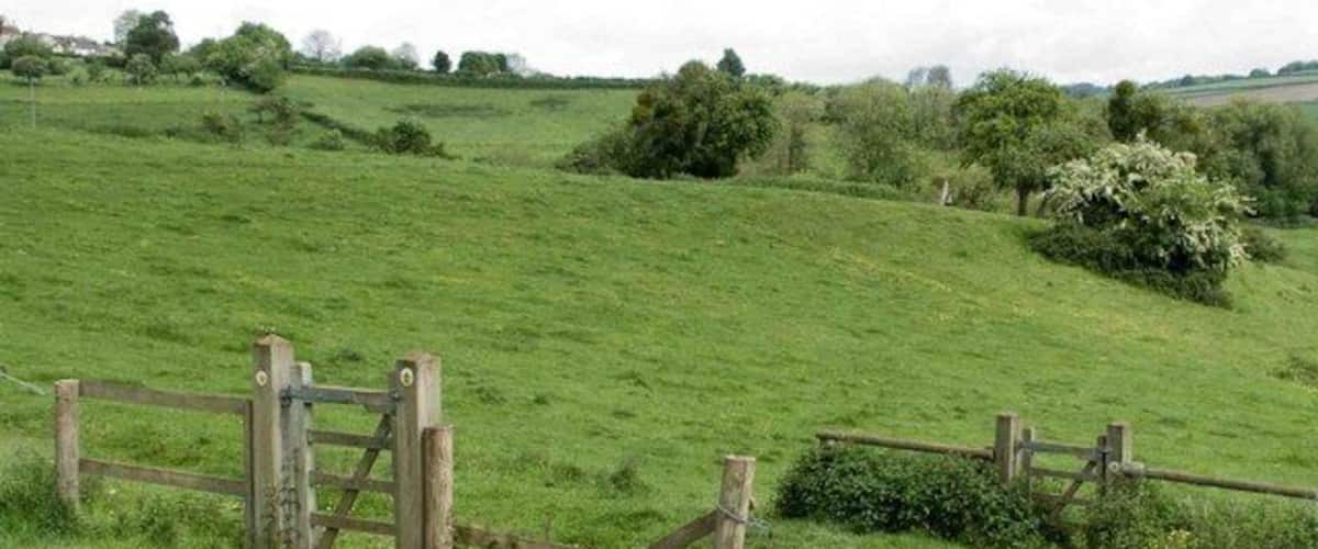 A rural landscape with rolling green hills, a wooden gate, and a fence.