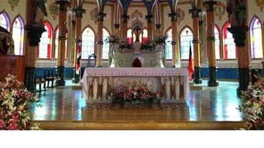 A church interior with ornate Gothic arches, stained glass windows, and a central altar.