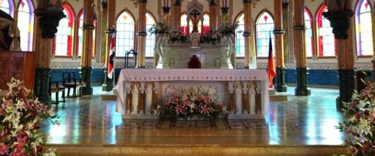 A church interior with ornate Gothic arches, stained glass windows, and a central altar.