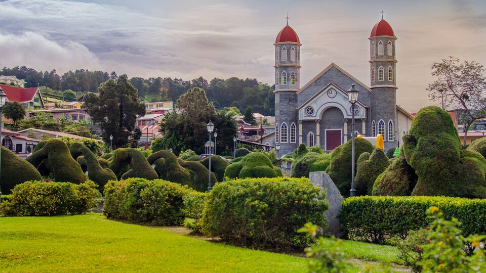 A church with two towers, surrounded by well-manicured hedges and a lush green lawn.
