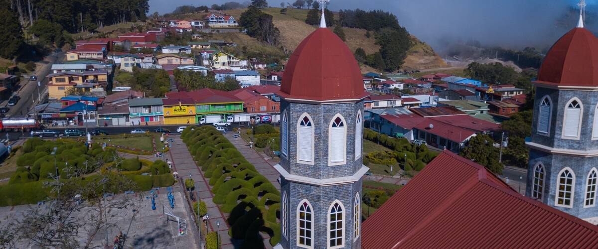 A town with two prominent red-roofed towers, a church, and a green park with neatly trimmed bushes.