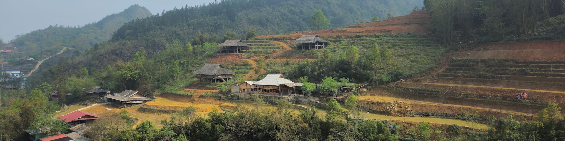 Terraced rice fields, traditional houses, and a waterfall in a hilly landscape.