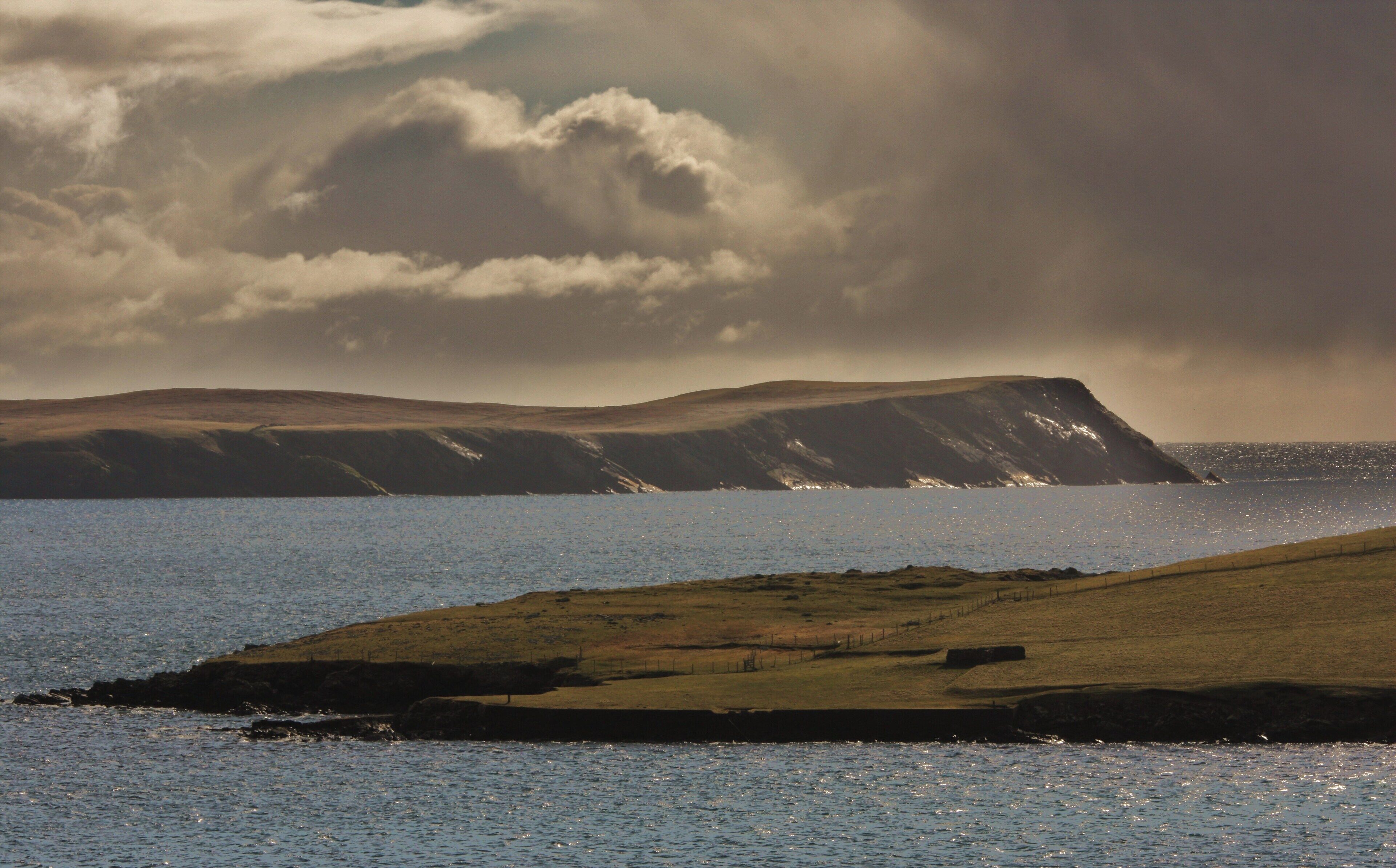 A coastal landscape with a grassy hill and a rocky cliff by the sea.