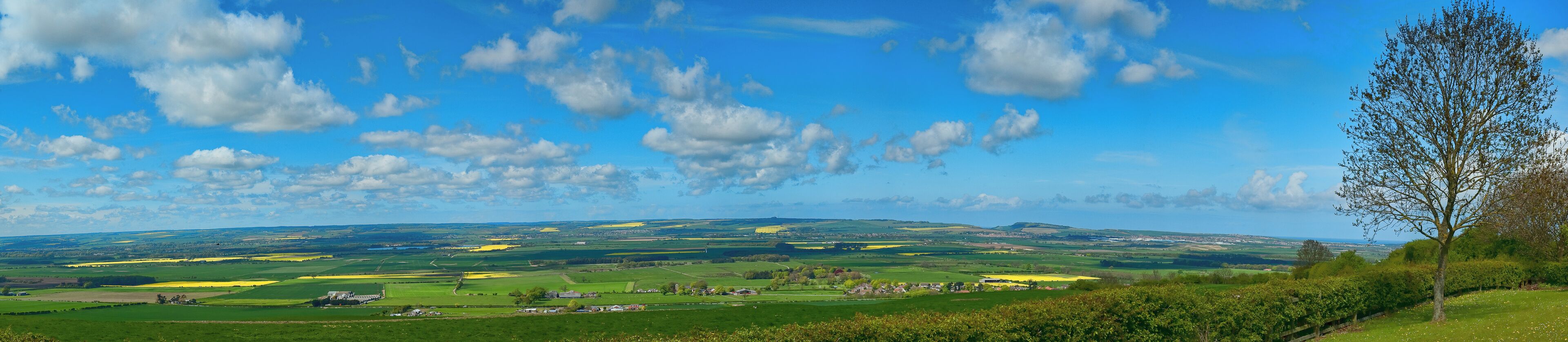 A rural landscape with rolling hills, fields, and scattered houses under a partly cloudy sky.