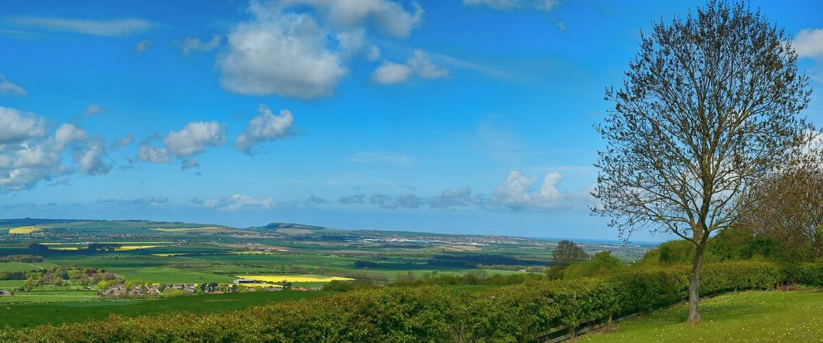 A rural landscape with rolling hills, fields, and scattered houses under a partly cloudy sky.