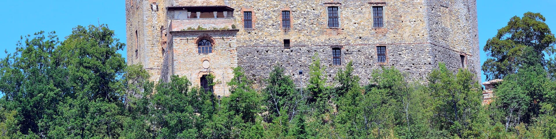 A historic stone castle with multiple towers and arched windows, surrounded by lush greenery.