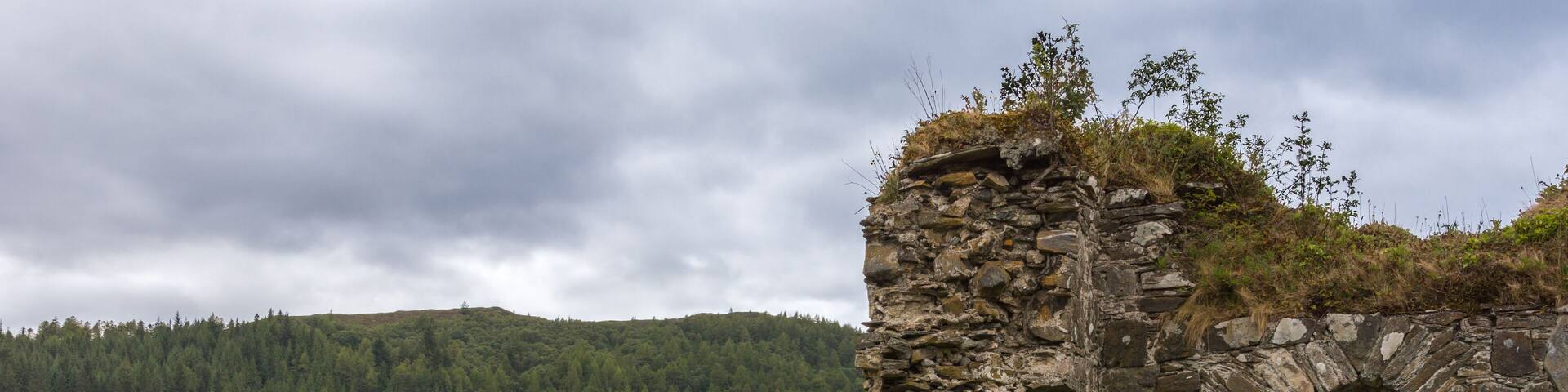Stromeferry, Scotland - June 10, 2012: Window in rock wall of Castle Strome ruins on green hill. Cloudscape and Loch Carron with motor boat seen in back. Mountains on opposite shore and horizon.