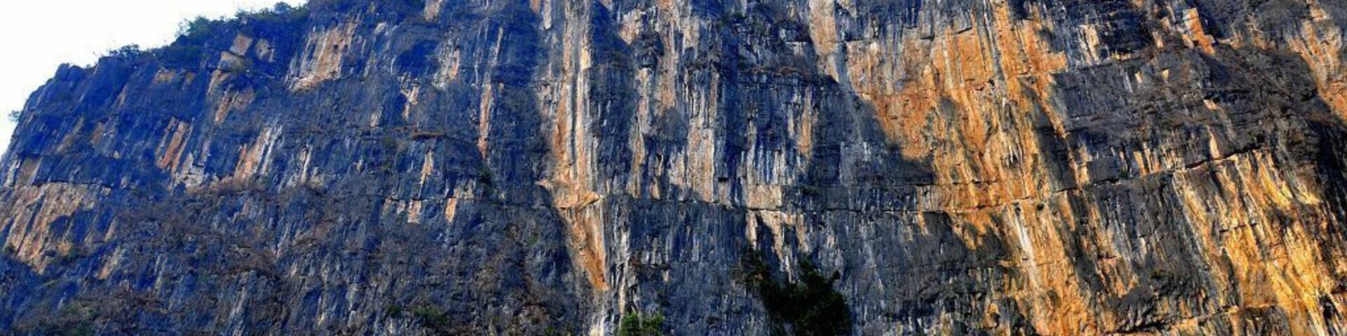 A towering cliff with vertical rock faces and sparse vegetation at its base.
