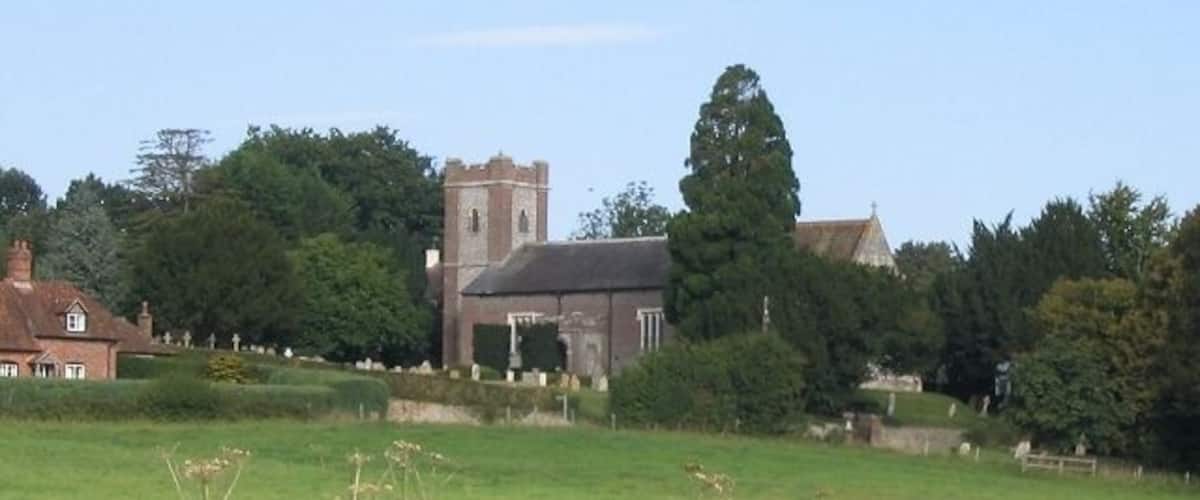A church with a tower, surrounded by greenery and a field.