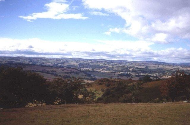 A rural landscape with rolling hills, a river, and scattered trees.