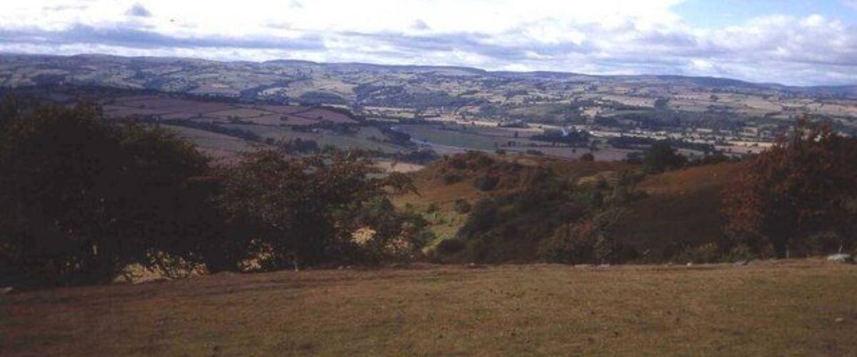 A rural landscape with rolling hills, a river, and scattered trees.