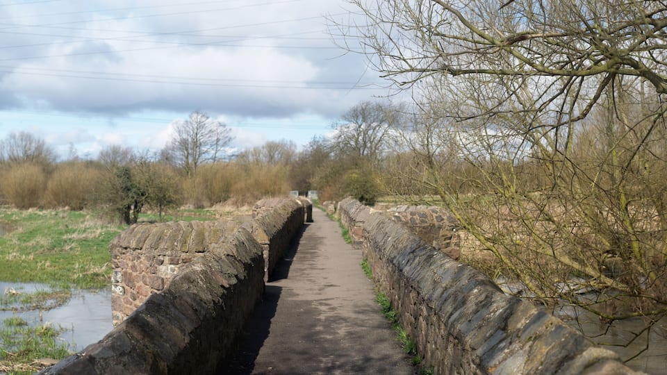 A narrow stone bridge over a canal with a pathway on either side.