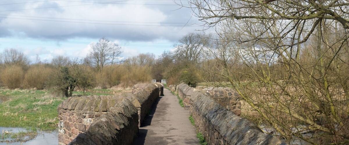 A narrow stone bridge over a canal with a pathway on either side.