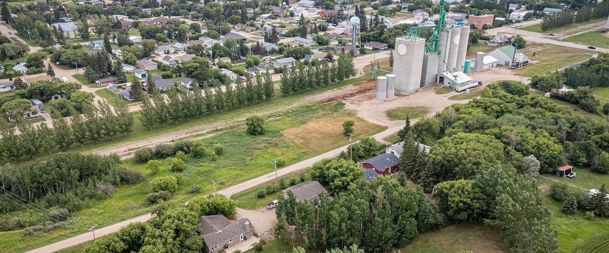 An aerial view of a rural town with a grain silo complex, residential houses, and surrounding fields.