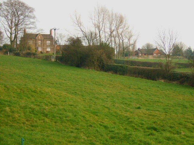 A grassy field with a large house and a smaller building in the background.