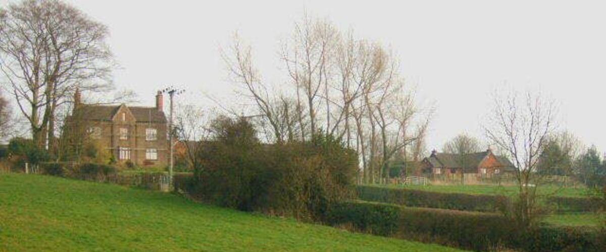 A grassy field with a large house and a smaller building in the background.