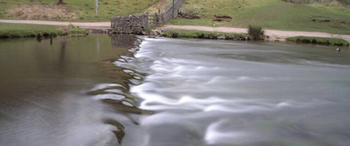 A river with smooth water flow, a stone bridge, and grassy banks.