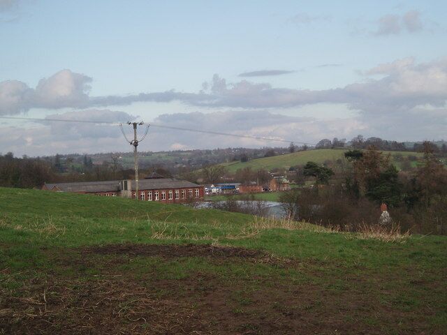 A rural landscape with a field, a small body of water, a red building, and a power line structure.