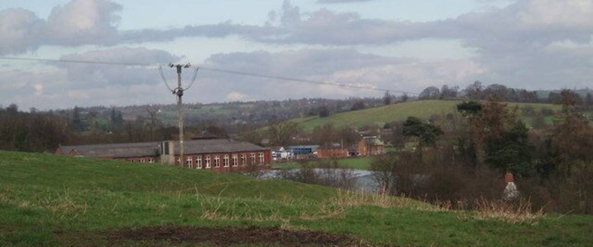 A rural landscape with a field, a small body of water, a red building, and a power line structure.