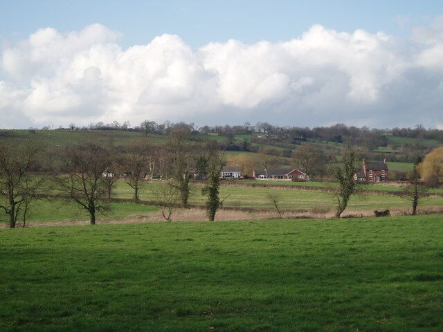 A rural landscape with green fields, scattered trees, and a distant house.