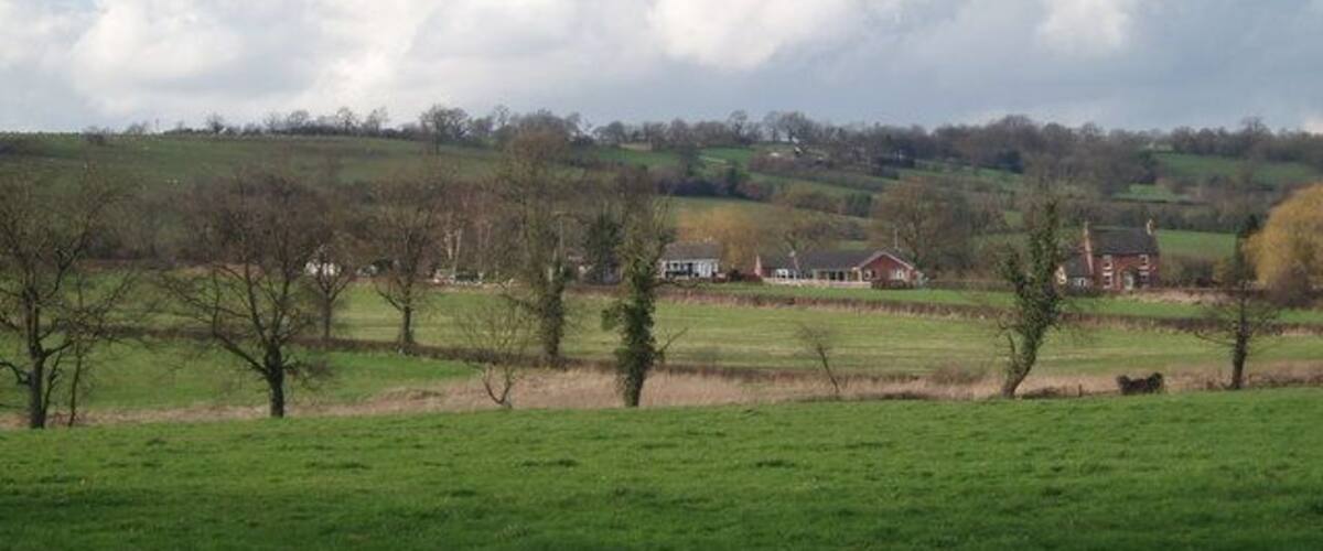 A rural landscape with green fields, scattered trees, and a distant house.