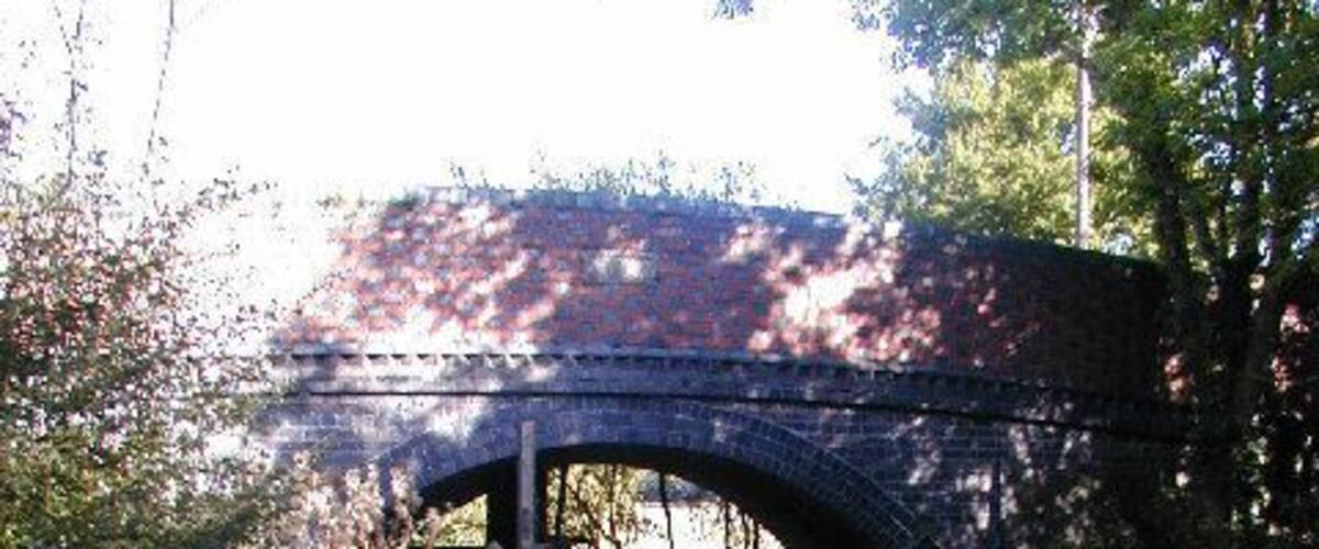 A stone bridge over a narrow waterway with green algae.