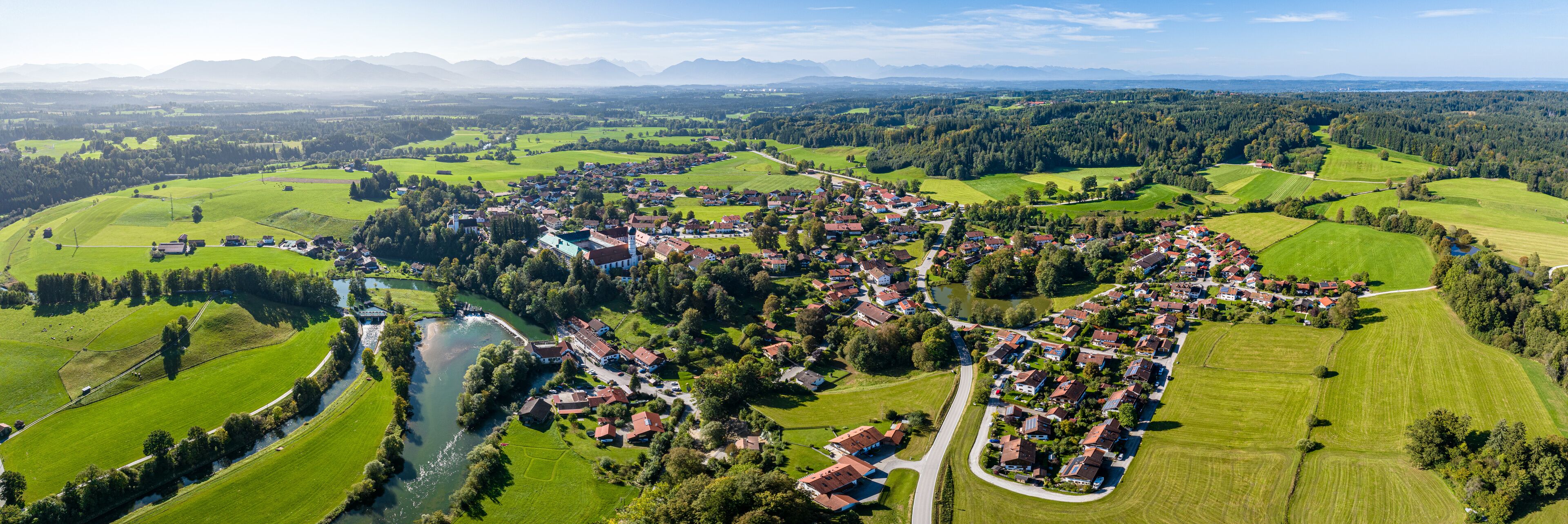A rural landscape with a river, green fields, and scattered houses.