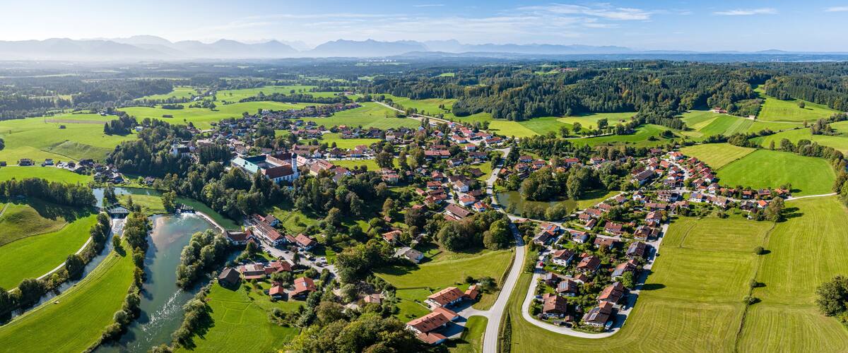 A rural landscape with a river, green fields, and scattered houses.