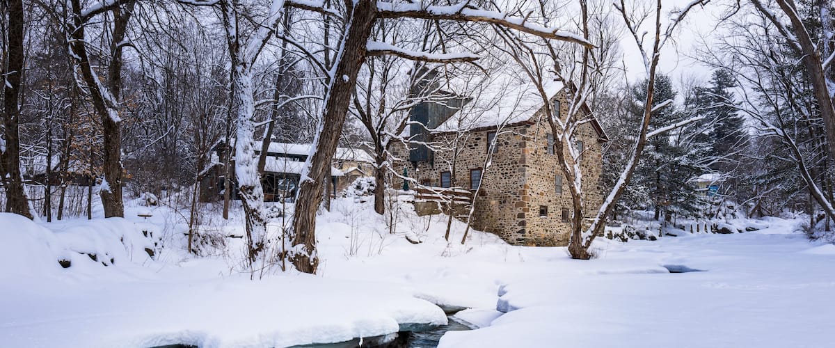 A stone house surrounded by snow-covered trees and a partially frozen stream.