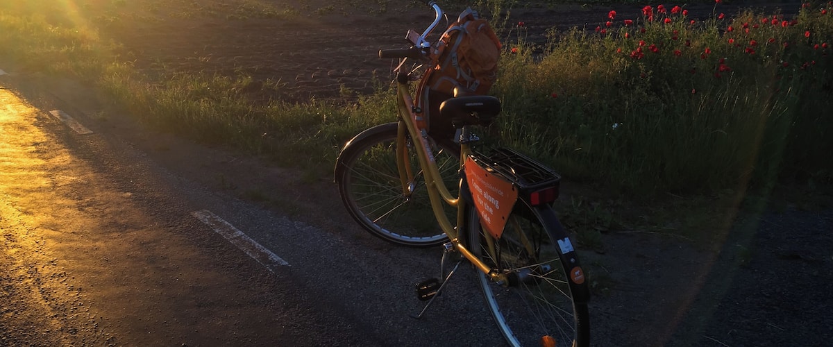 A bicycle parked on a rural road with a sunset in the background.