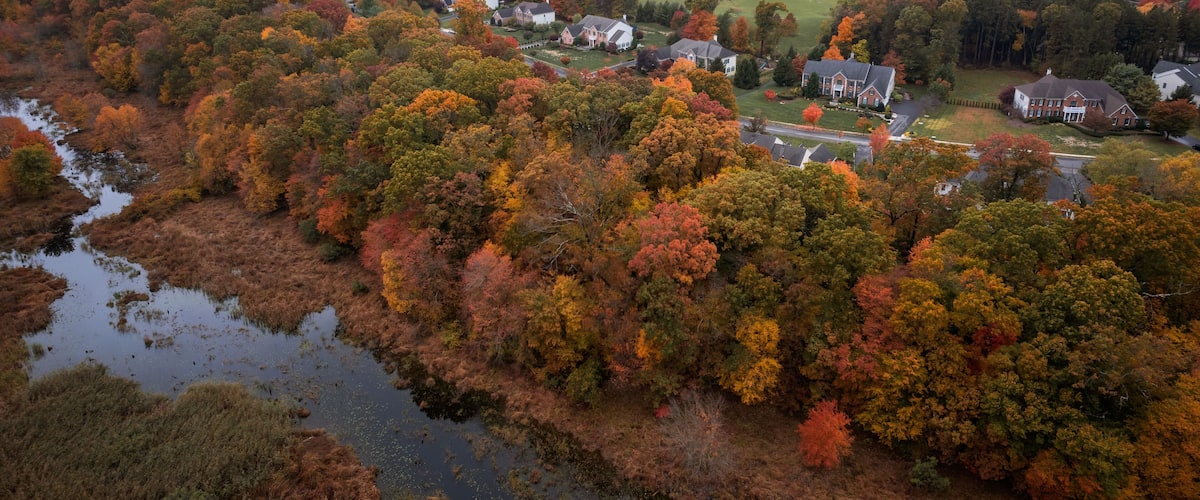 An aerial view of a rural area with autumn-colored trees, a river, and scattered houses.