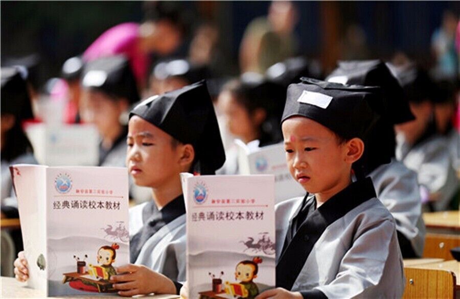Students in graduation gowns and caps holding books.