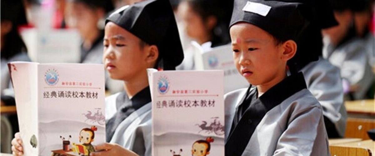 Students in graduation gowns and caps holding books.