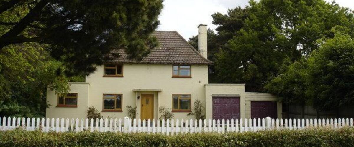 A two-story house with a white picket fence, a brown door, and a red garage door.