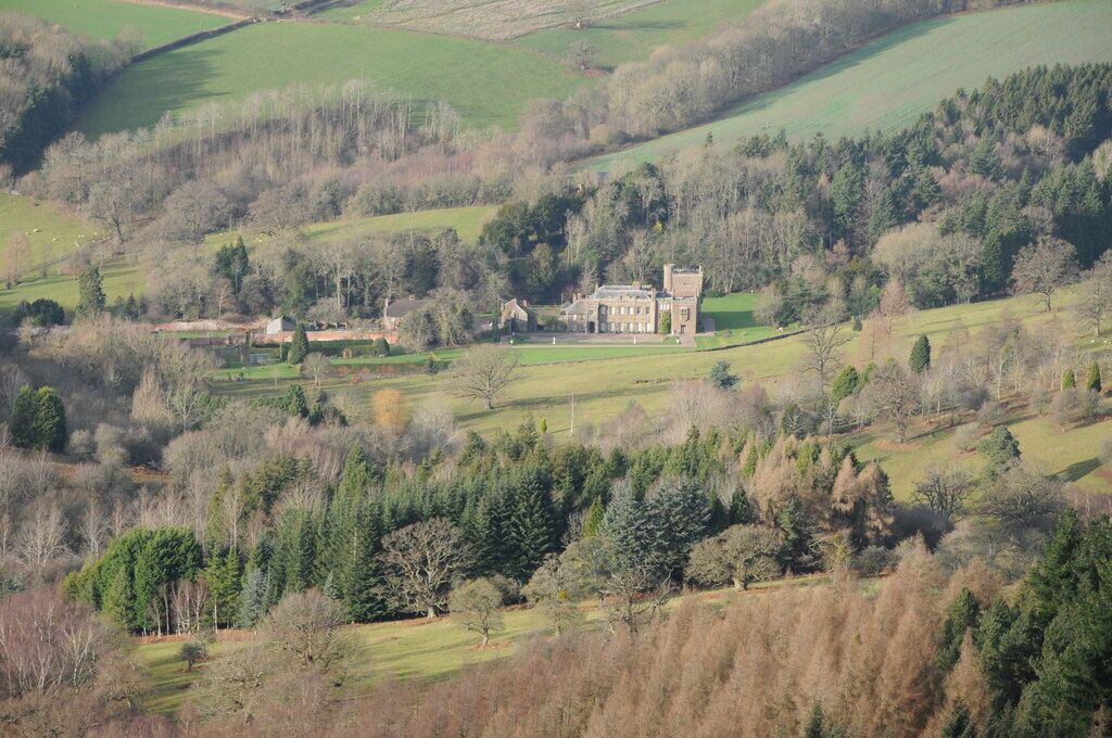 A large estate with a prominent manor house surrounded by rolling green fields and dense forests.
