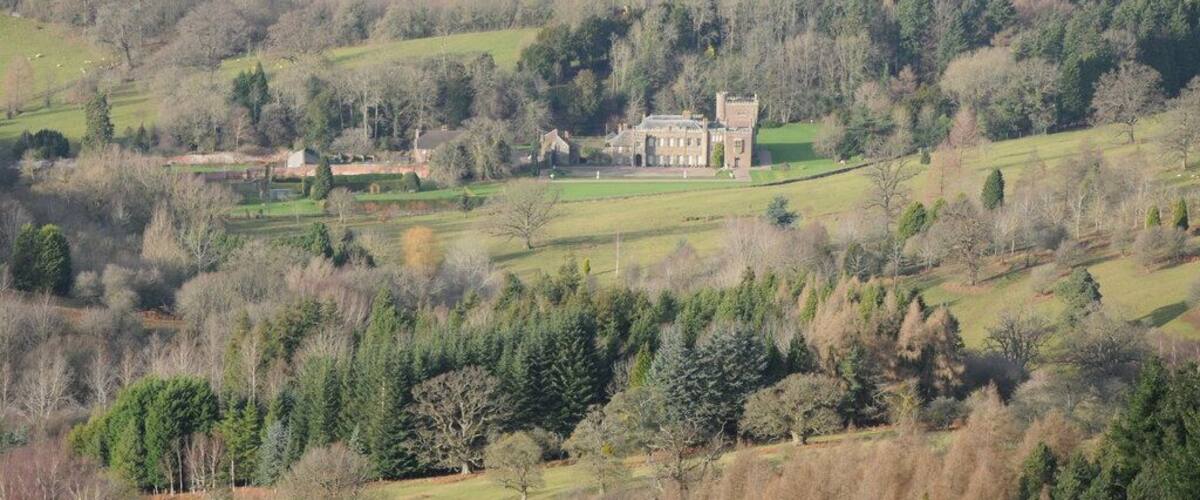 A large estate with a prominent manor house surrounded by rolling green fields and dense forests.