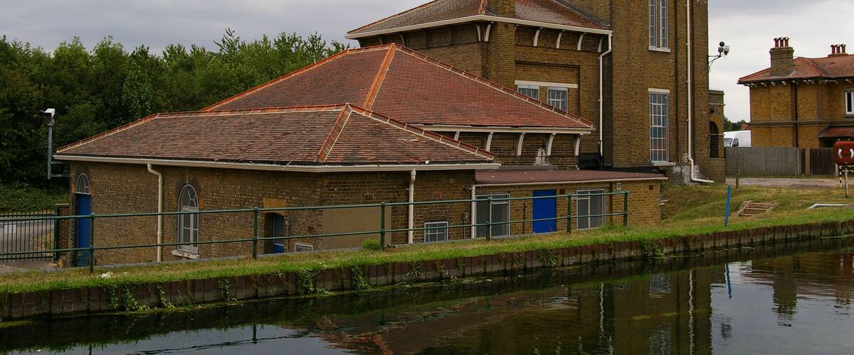 A brick building with a red-tiled roof and a tower, situated beside a canal.