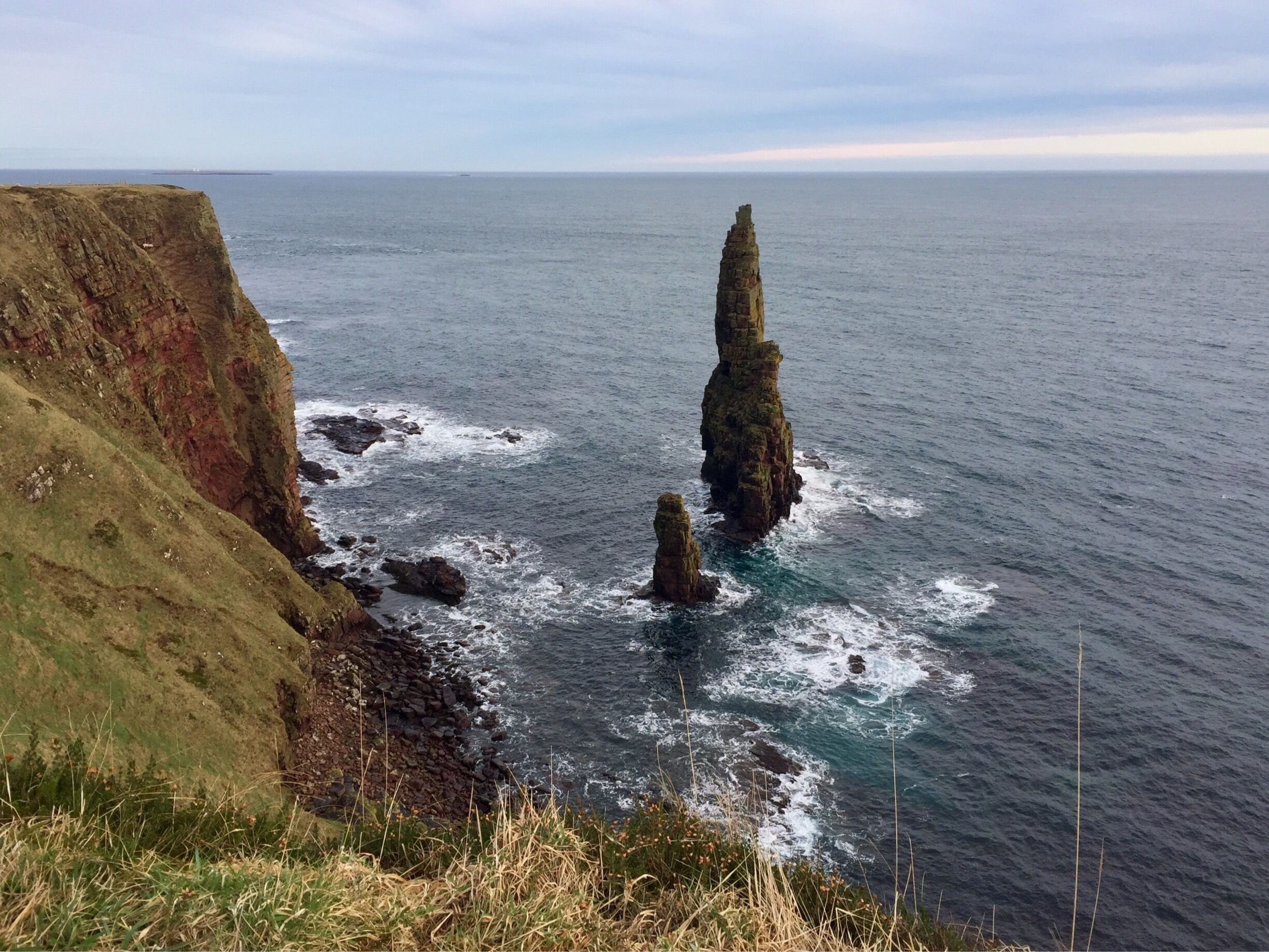 A coastal landscape with rocky cliffs and two prominent rock formations in the sea.