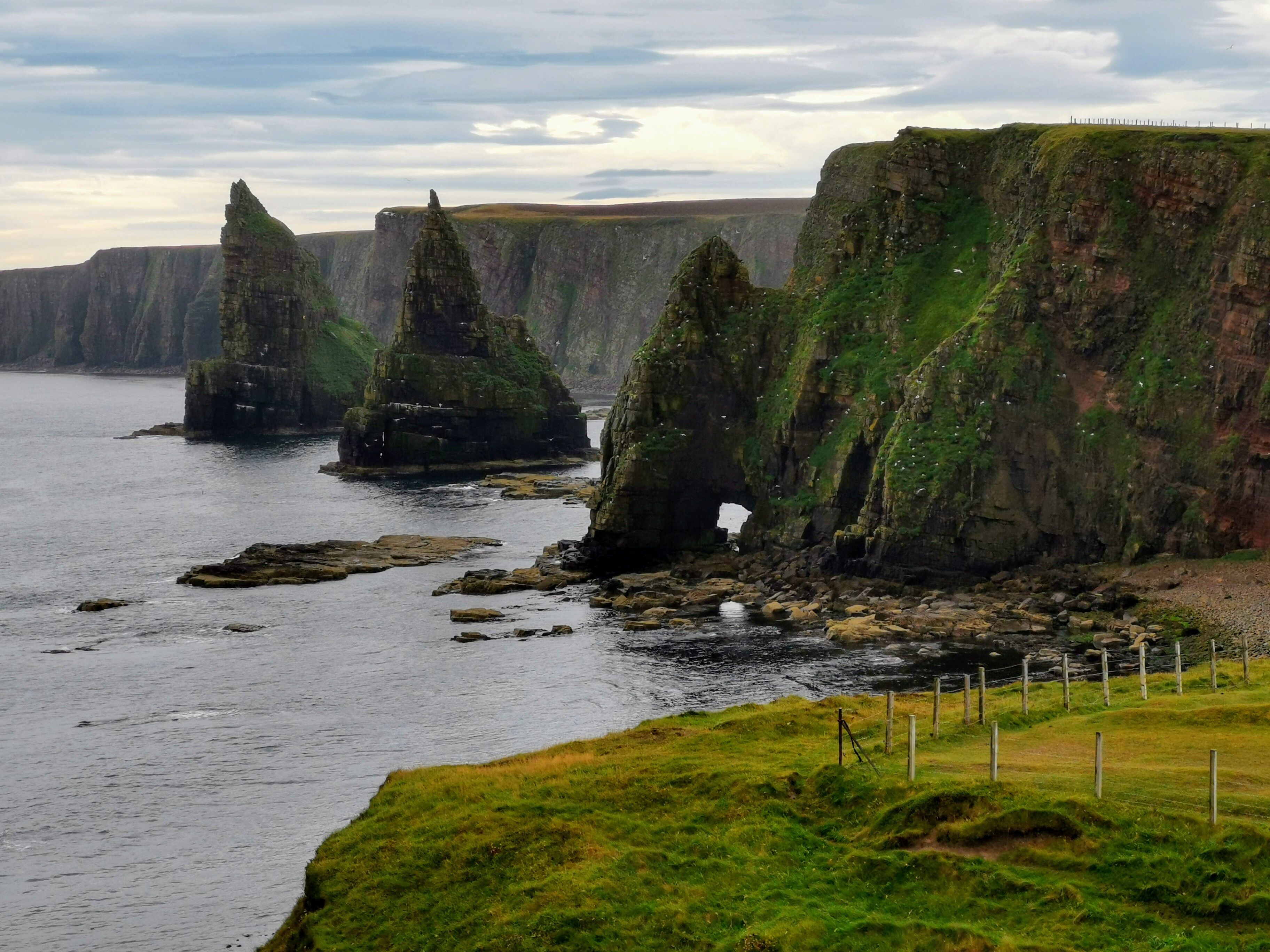 A coastal landscape with prominent rock formations and a grassy foreground.