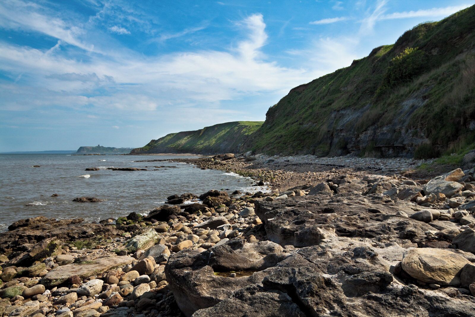 A rocky shoreline with large boulders and a grassy cliff.