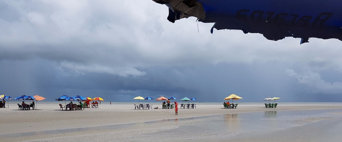 A beach with umbrellas and chairs, a person walking, and a cloudy sky.