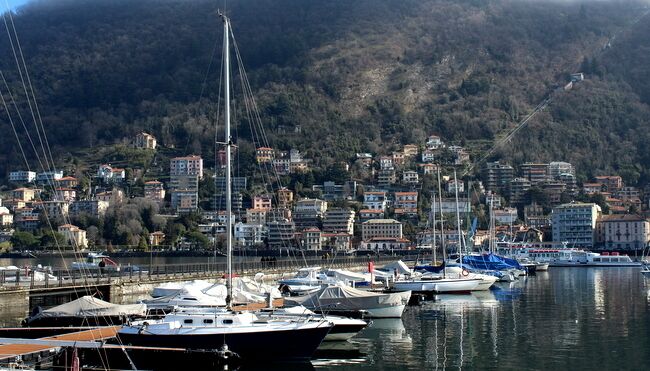 A marina with several boats docked, a hillside town in the background, and a clear sky.