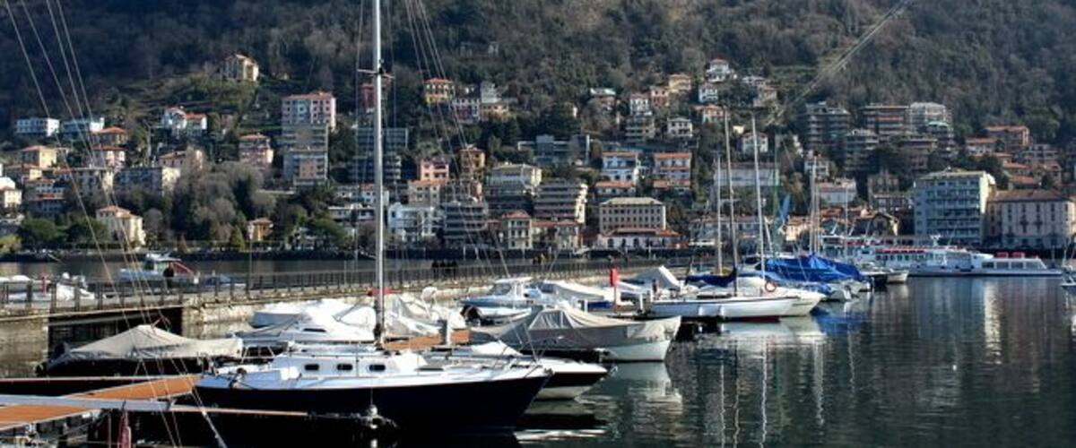 A marina with several boats docked, a hillside town in the background, and a clear sky.