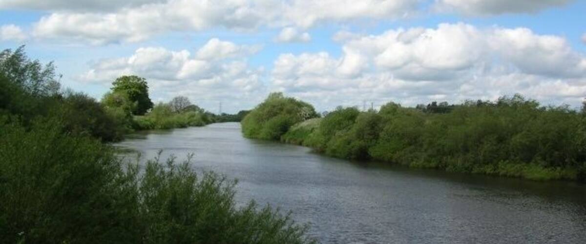 A river flanked by dense greenery under a partly cloudy sky.