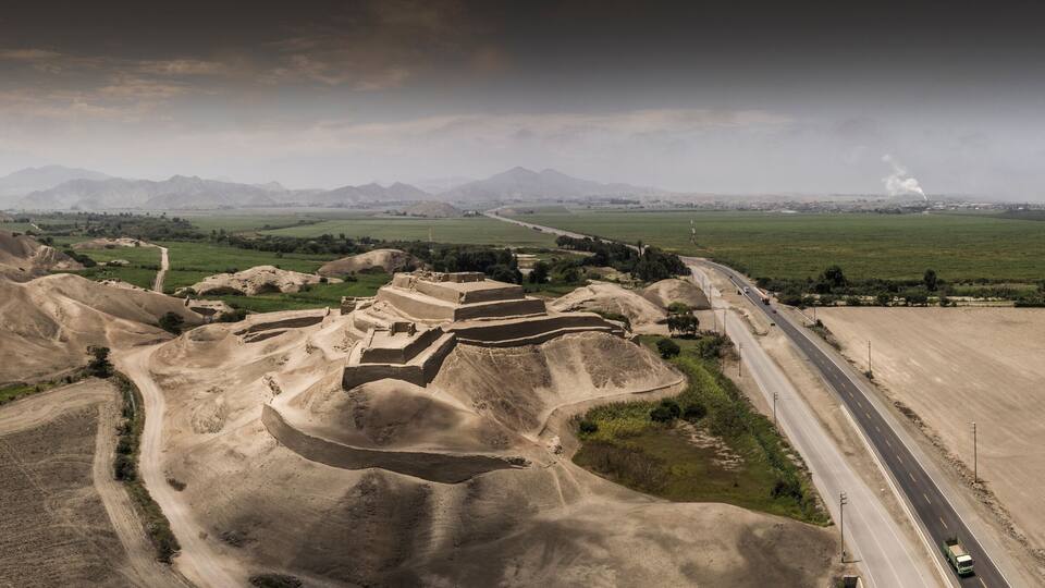 A vast desert landscape with a winding road, distant mountains, and a small settlement with ancient ruins.