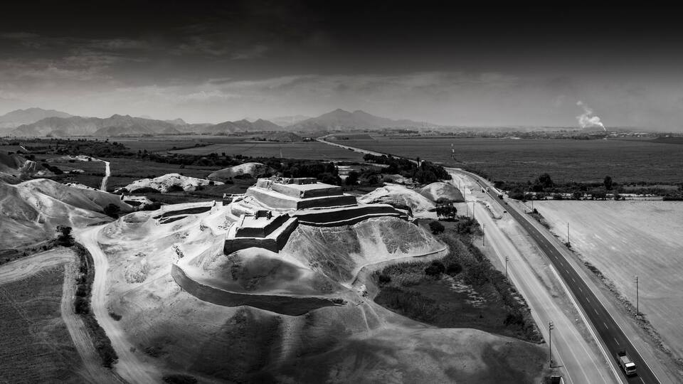 An aerial view of a mountainous landscape with terraced fields, a winding road, and distant mountains.