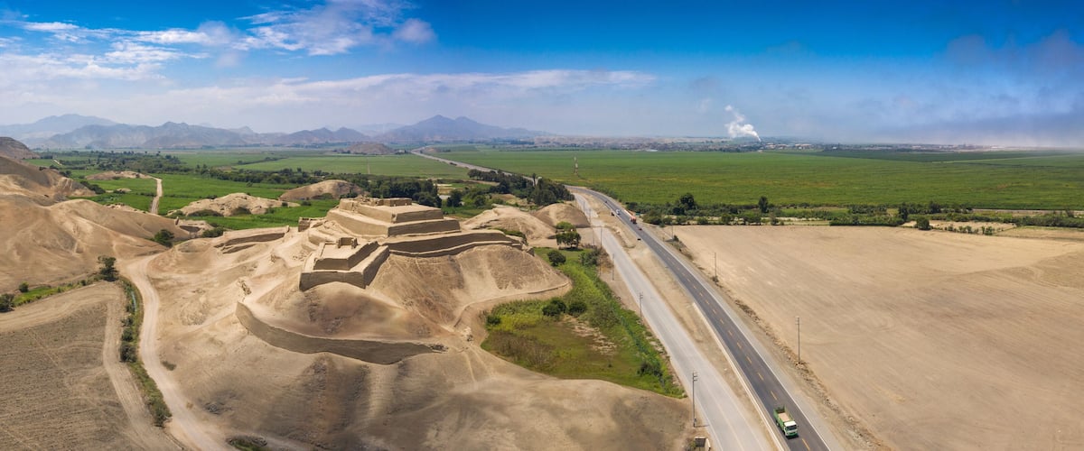 A mountainous landscape with a road, green fields, and distant mountains.