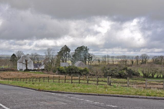A rural landscape with a road, a wooden fence, and houses in the background.