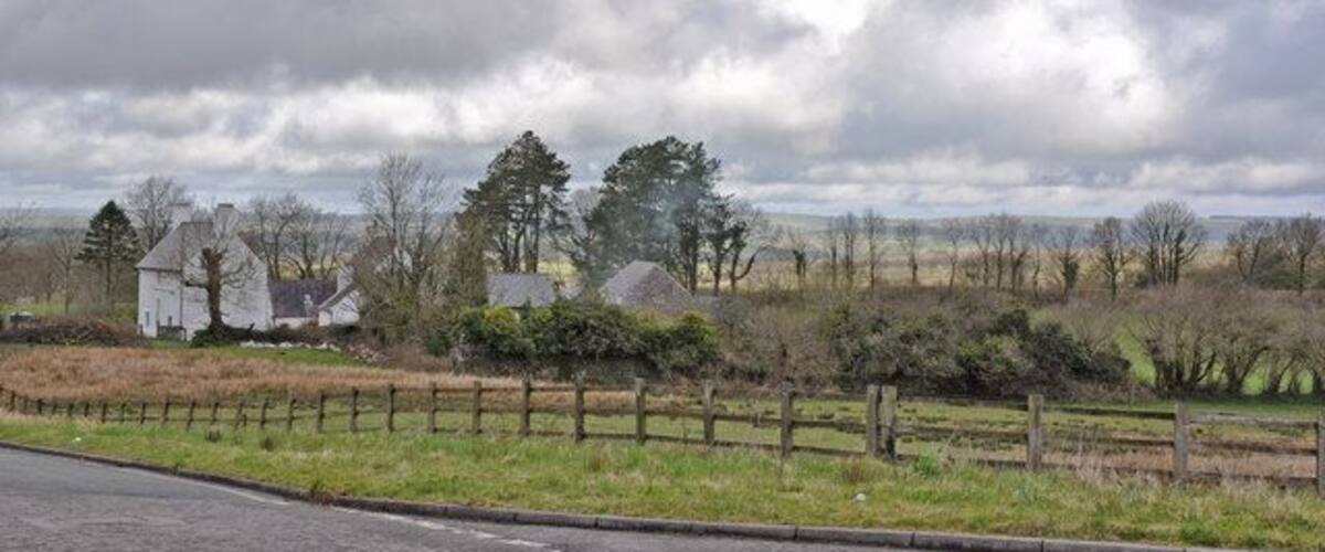A rural landscape with a road, a wooden fence, and houses in the background.
